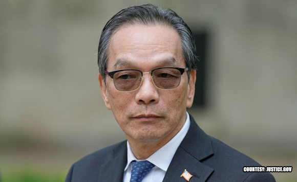 Portrait of an Asian man in a dark suit and blue tie wearing sunglasses, outdoors with a neutral background; a small lapel pin is visible.